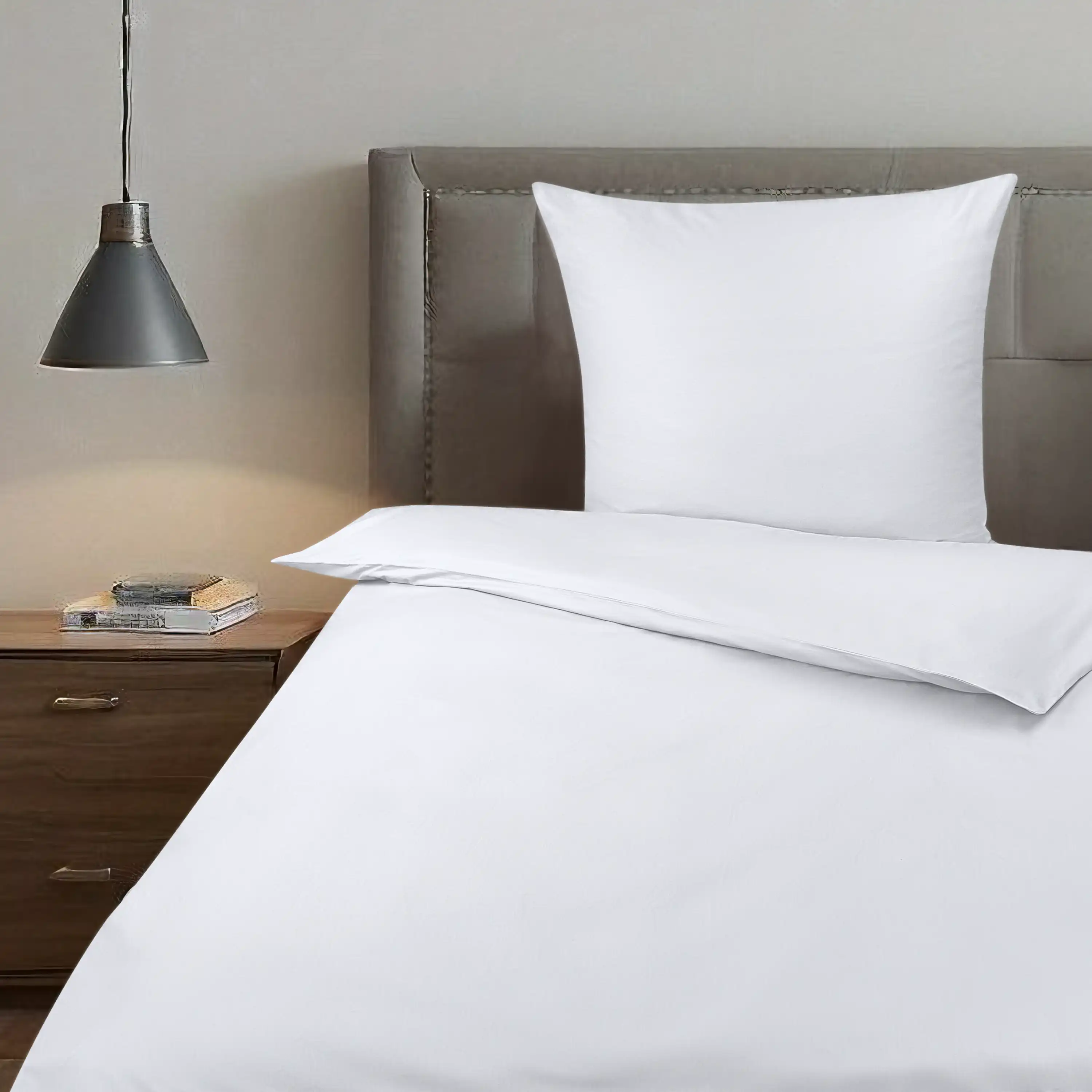 Professionelle Produktfotografie von weißer Bettwäsche auf einem Bett mit grauem Kopfteil und Nachttischlampe.