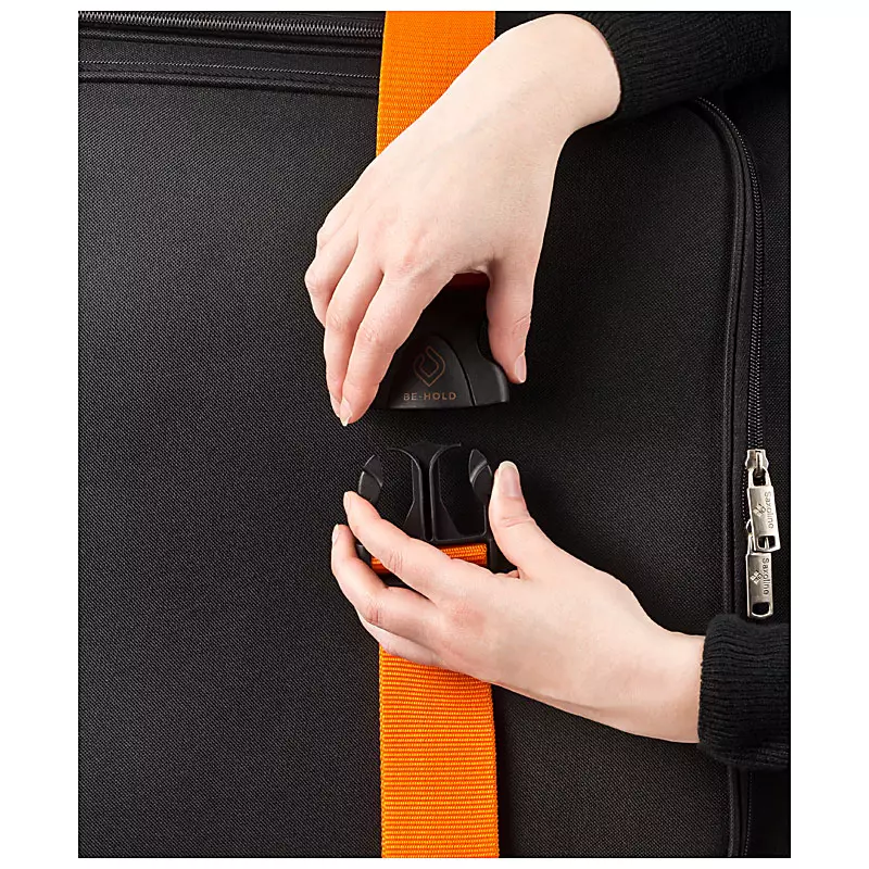 Hände schließen einen orangefarbenen Kofferriemen mit Schnalle. Professionelle Produktfotografie durch PRO-ducto GmbH für hochwertige Produktbilder.