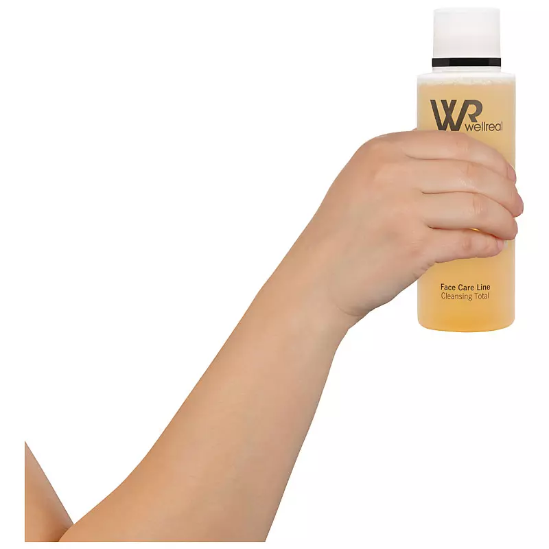Eine Hand hält eine Flasche Wellreal Face Care Line Cleansing Total für professionelle Produktfotos von PRO-ducto GmbH vor weißem Hintergrund.