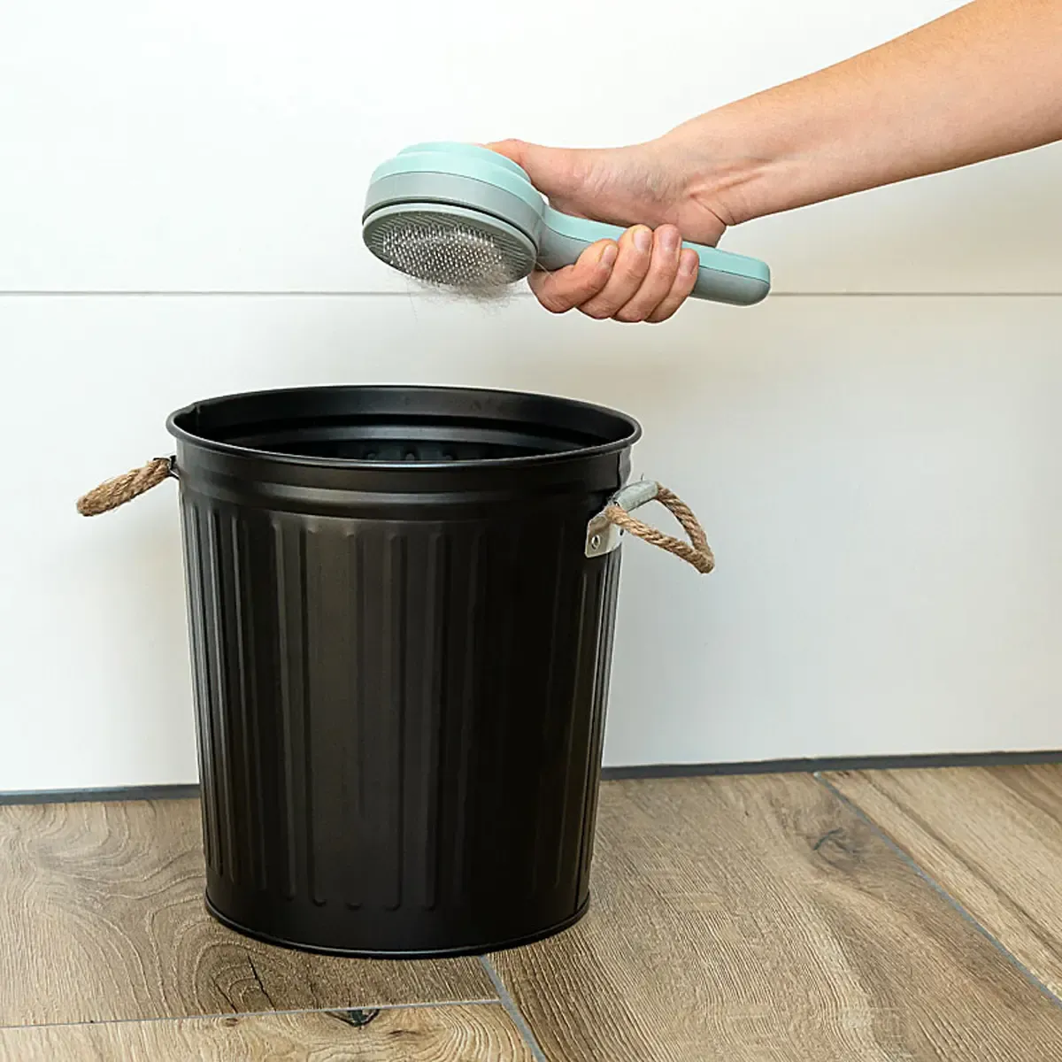 Eine Hand hält eine Tierhaarbürste über einen schwarzen Mülleimer. Professionelle Produktfotos zeigen, wie man Tierhaare effizient entfernen kann. PRO-ducto GmbH