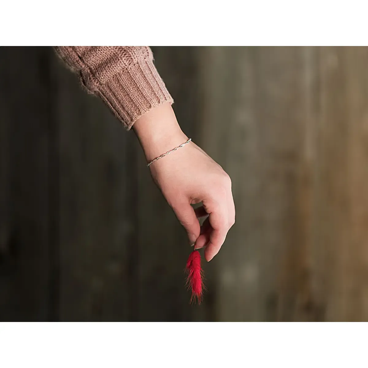 Professionelle Produktfotografie: Eine Hand in einem beigen Strickpullover hält eine rote Feder. Ideal für hochwertige Produktbilder und Textilfotografie. PRO-ducto GmbH